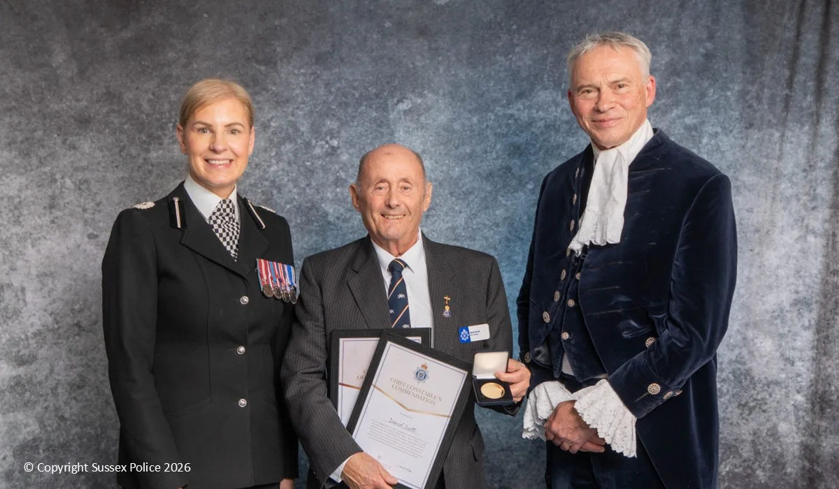 David Scott holding his Chief Constable's Commendation certificate and medal, standing between Assistant Chief Constable Rosie Ross and the High Sheriff of West Sussex.